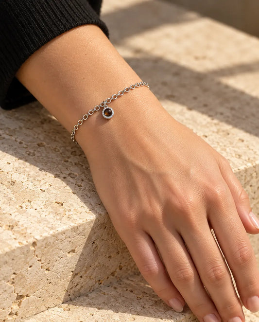Vrouw draagt de zilverkleurige armband met rond zirkonia-bedeltje en foto erin om haar pols in warm zonlicht
