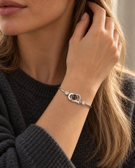 Vrouw strijkt met haar hand door haar haar en draagt de zilverkleurige armband met open hartje