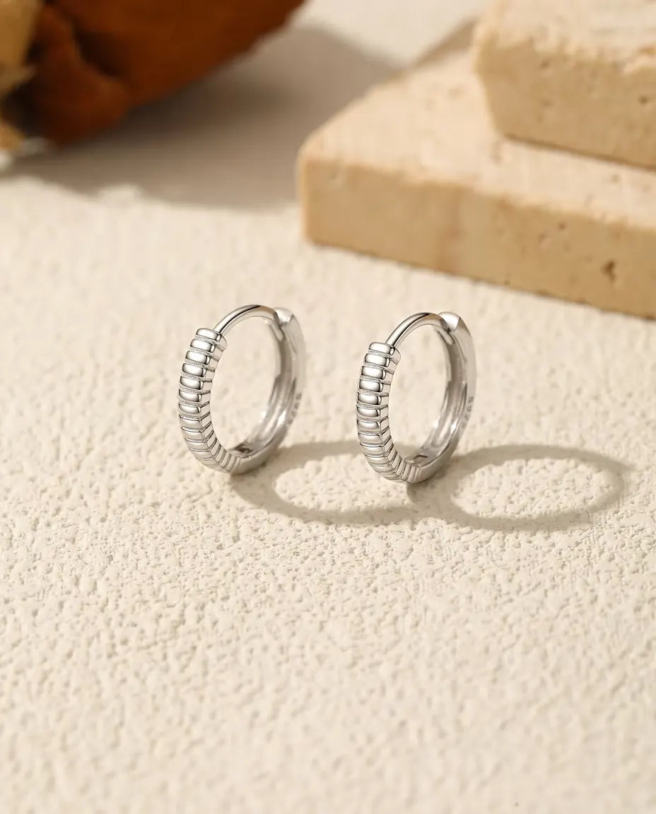 Huggie Creolen met Ribbels in 925 Sterling Zilver - het paar naast elkaar op een licht gestructureerd oppervlak