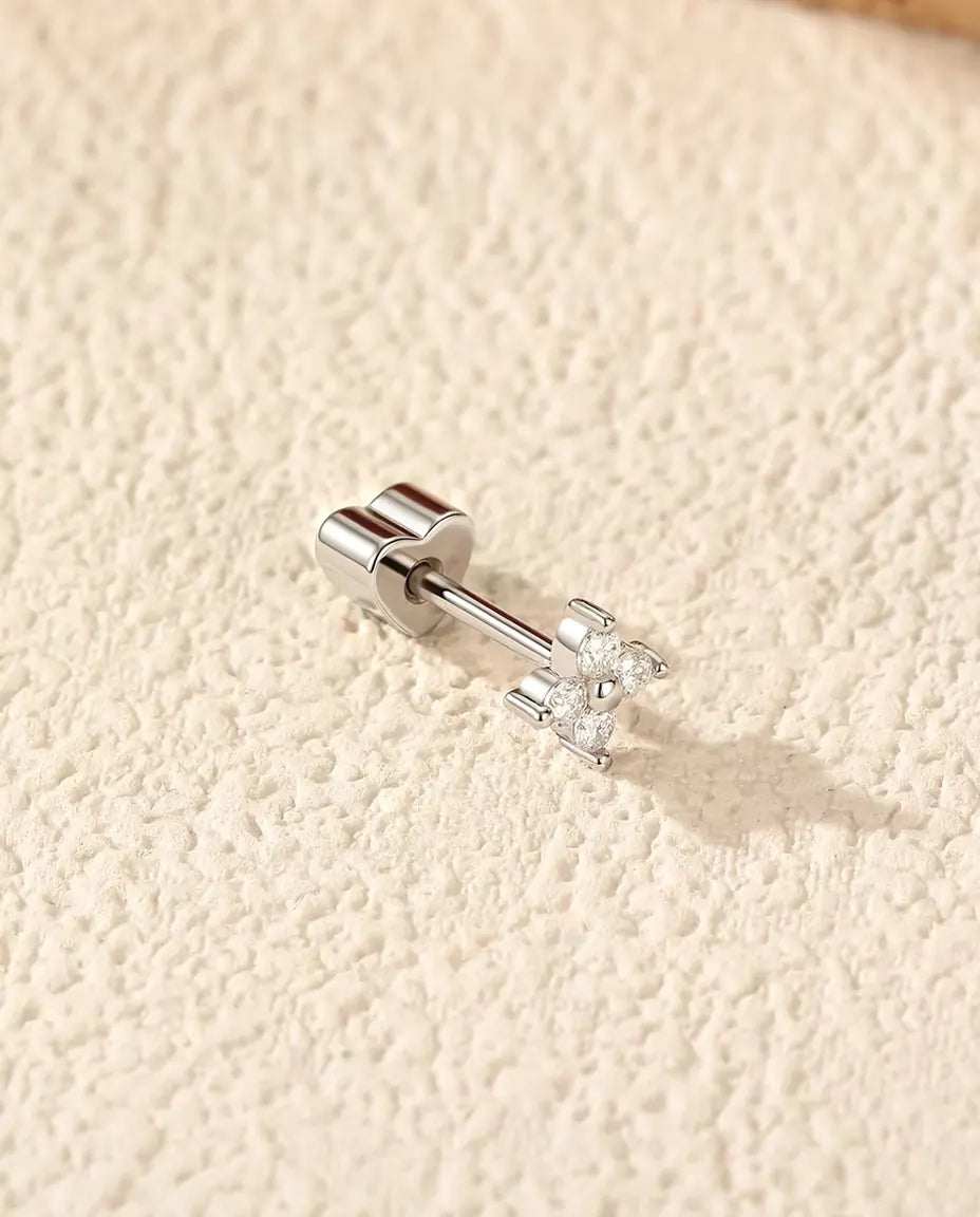 Moissanite Oorknopjes Klavertje Vier in 925 Sterling Zilver - op zijn kant op een licht gestructureerd oppervlak, hartvormig achterkantje op de stift