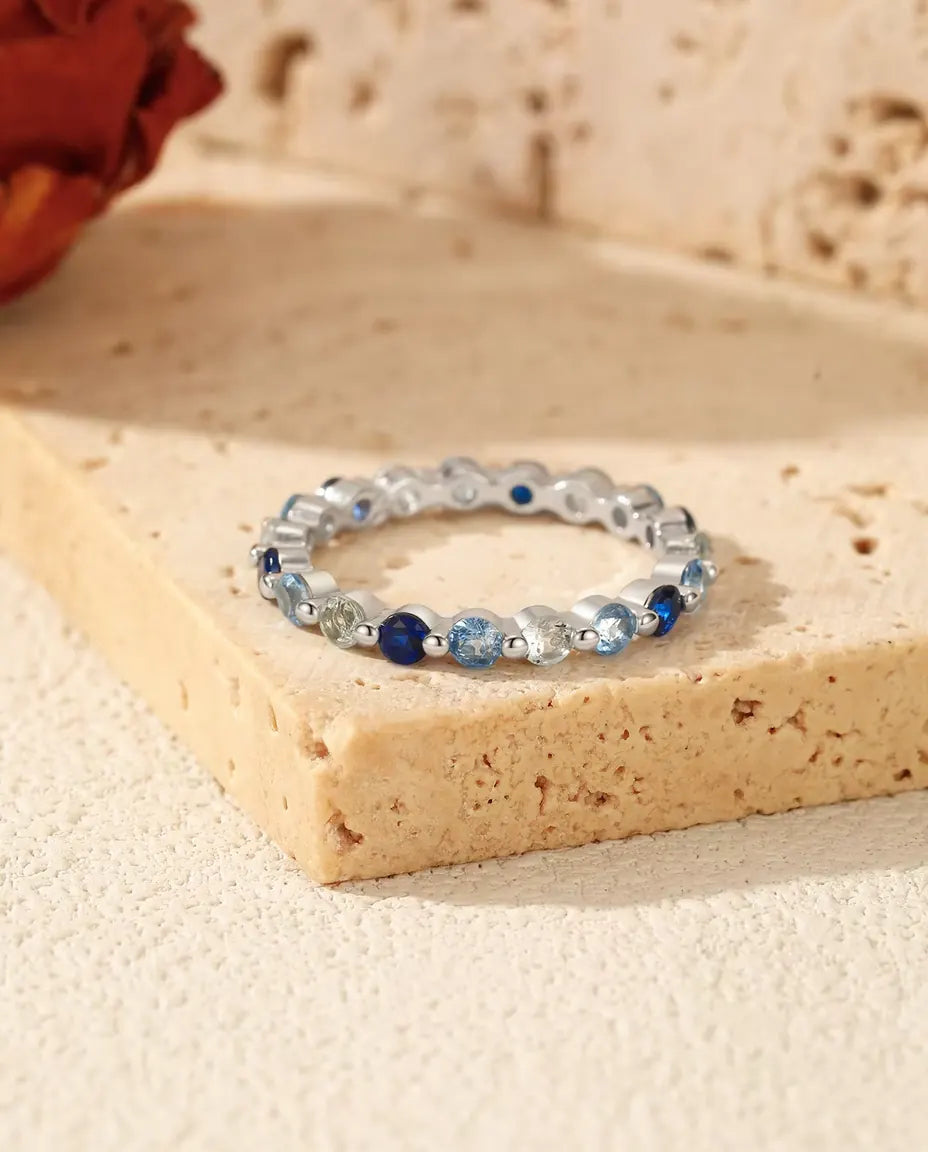 Ring met Blauwe Zirkonia Rondom in 925 Sterling Zilver - liggend op een blok travertijn