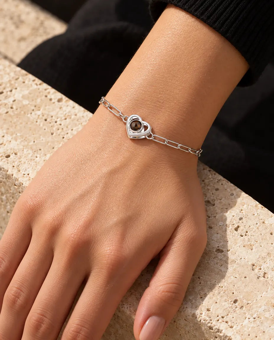 Vrouw draagt de zilverkleurige armband met dubbel hart en foto erin om haar pols in warm zonlicht