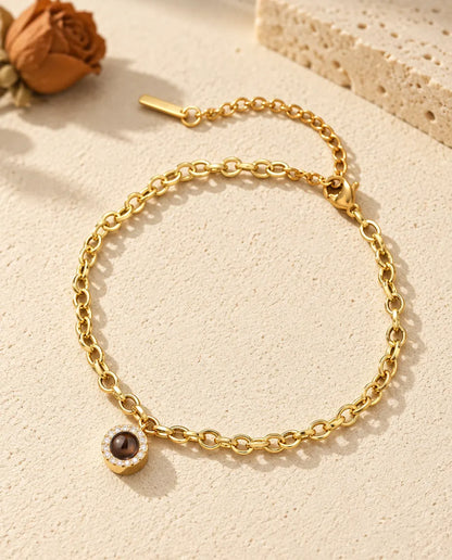 Goudkleurige armband met rond zirkonia-bedeltje en foto erin, liggend op crèmekleurig gips