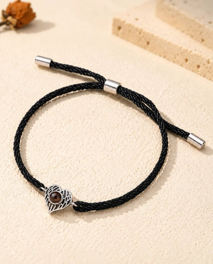 Armband met foto erin: zilverkleurig hart van engelenvleugels aan een zwart koord, op crèmekleurig gips