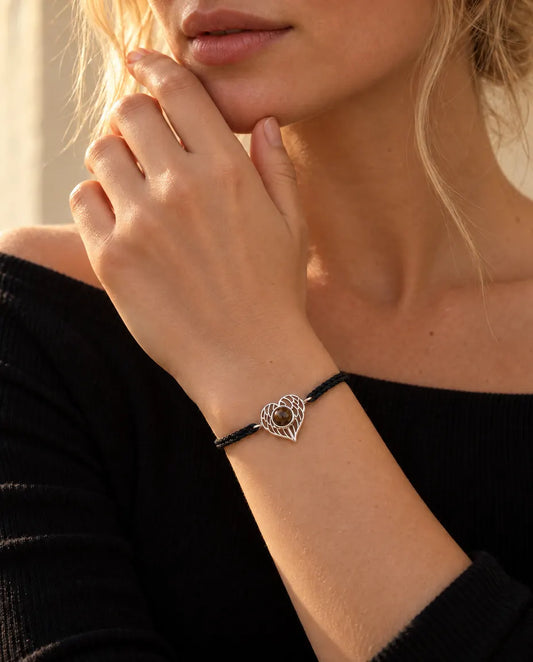 Vrouw met haar vingertoppen bij haar kaaklijn draagt de zilverkleurige armband met engelenvleugelhart