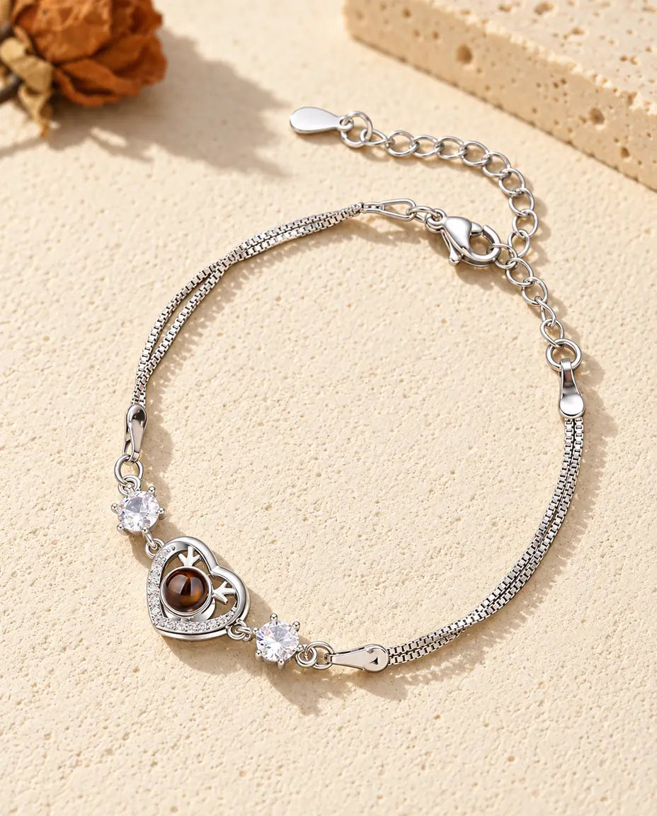 Armband met foto erin: zilverkleurig hartje met gewei en twee zirkonia aan een dubbele ketting, op crèmekleurig gips