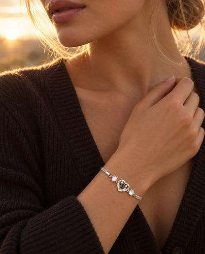 Vrouw raakt de hals van haar donkere gebreide top aan en draagt de zilverkleurige armband met het geweihartje