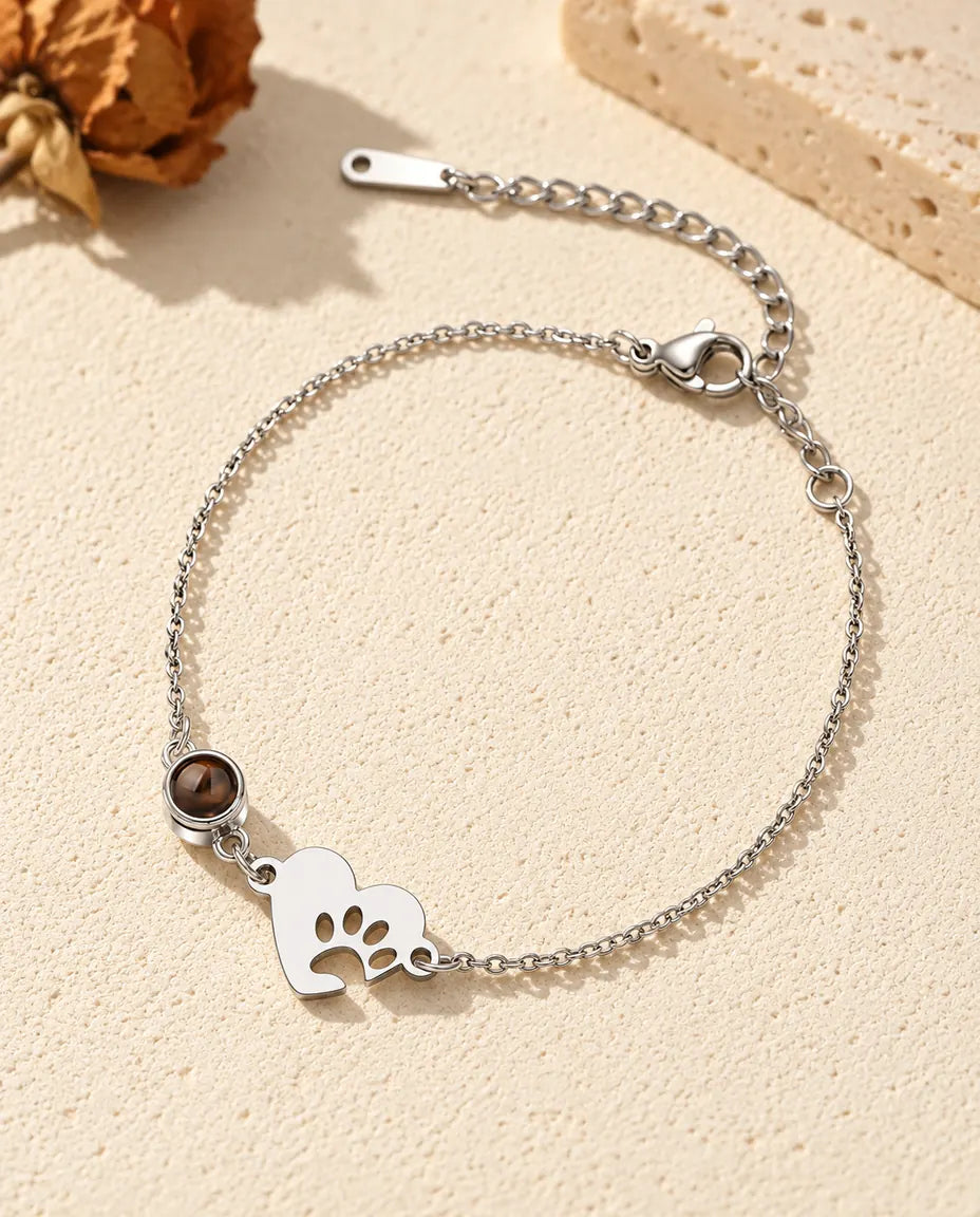 Armband met foto erin: zilverkleurig hartje met pootafdruk en projectiesteentje aan een fijne ketting, op crèmekleurig gips