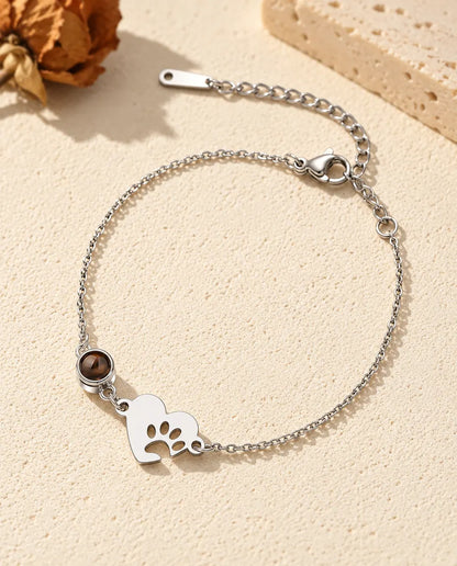 Armband met foto erin: zilverkleurig hartje met pootafdruk en projectiesteentje aan een fijne ketting, op crèmekleurig gips
