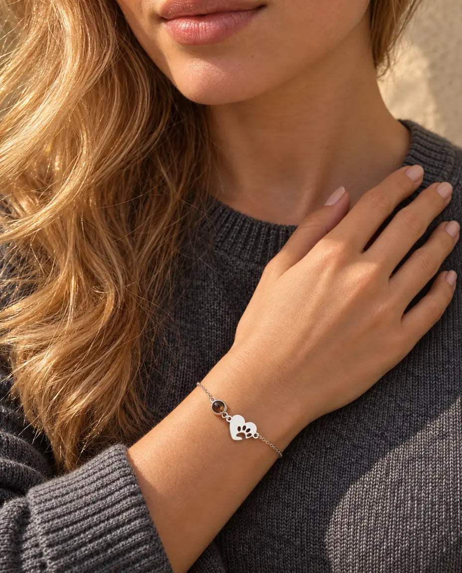 Vrouw met haar vingertoppen bij het sleutelbeen draagt de zilverkleurige armband met pootafdrukhartje