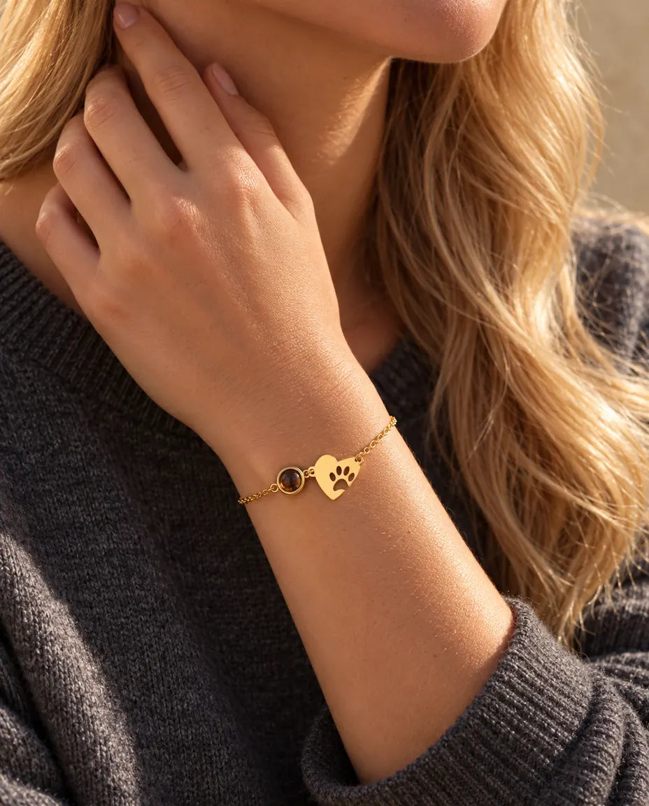 Close-up van de goudkleurige armband met pootafdrukhartje om een pols, vingertoppen langs de hals