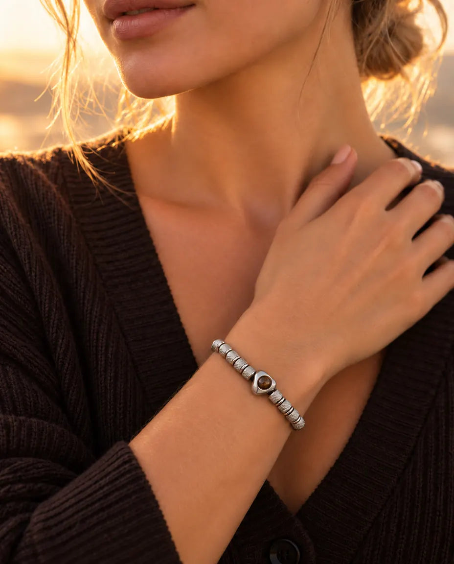 Vrouw met haar hand bij haar sleutelbeen draagt de zilverkleurige kralenarmband met hartkraal
