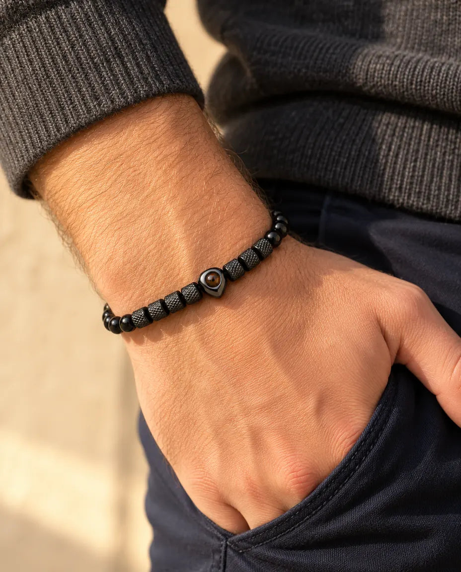 Man draagt de zwarte kralenarmband met hartkraal en foto erin, met zijn duim in zijn broekzak gehaakt