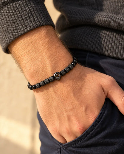 Man draagt de zwarte kralenarmband met hartkraal en foto erin, met zijn duim in zijn broekzak gehaakt