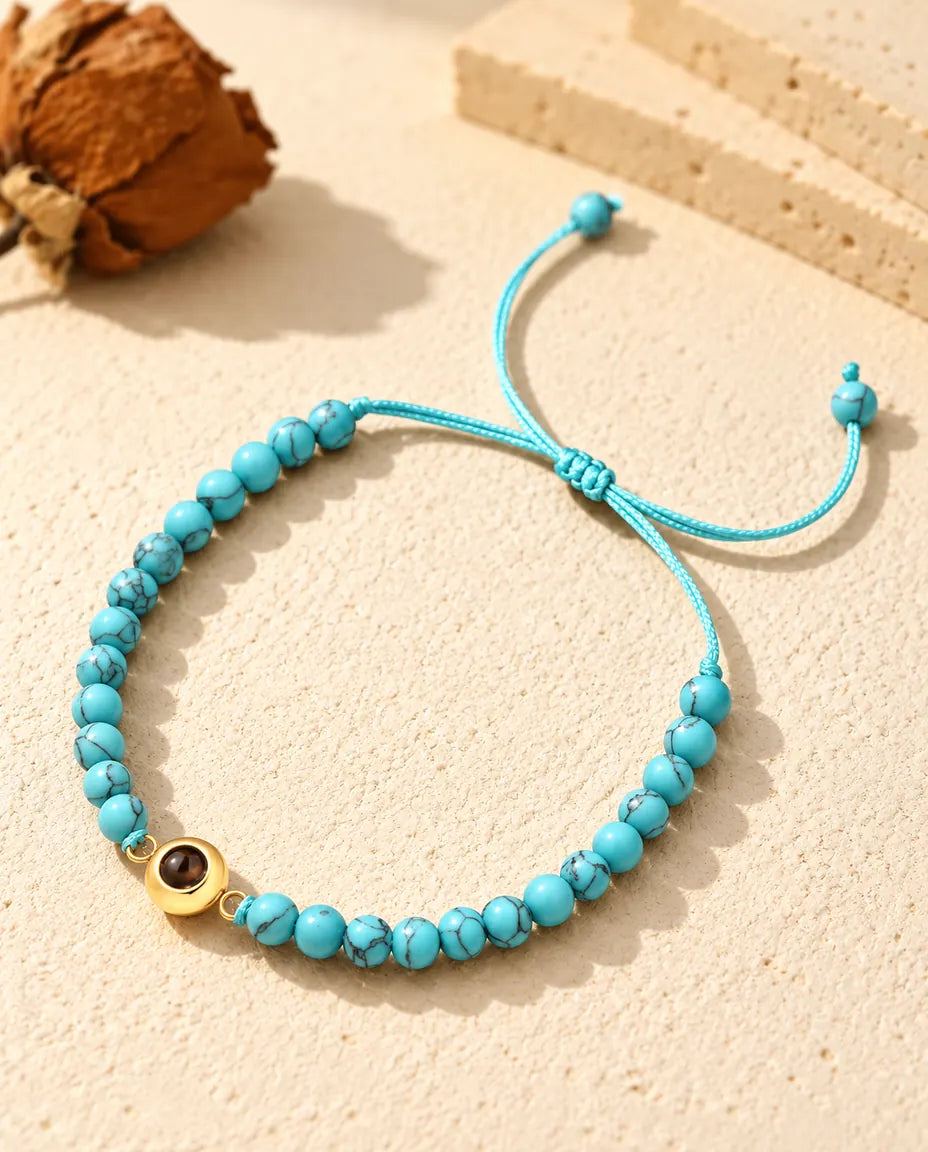 Gepersonaliseerde kralenarmband met foto erin: blauw gemarmerde kralen en een goudkleurige ringbedel op crèmekleurig gips