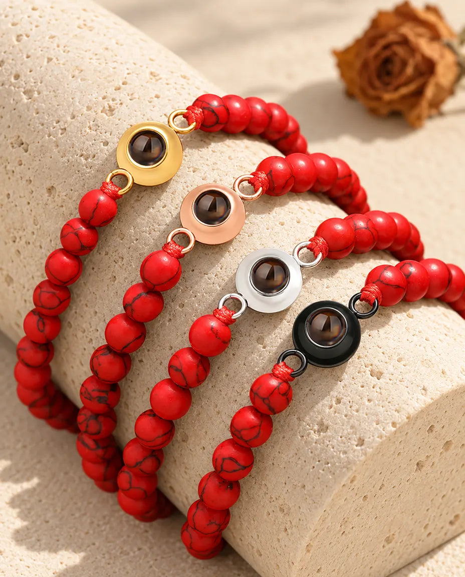 Rood gemarmerde kralenarmbanden met foto erin in vier bedelkleuren op een blok travertijn