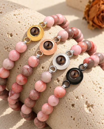 Roze gespikkelde kralenarmbanden met foto erin in elke bedelkleur, uitgestald op travertijn