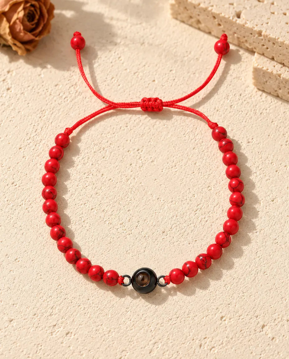 Bovenaanzicht van de rode kralenarmband met foto erin, een zwarte ringbedel en de schuifknoop