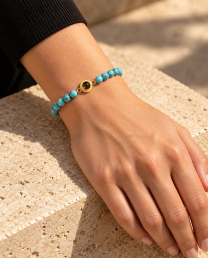 Vrouw draagt de blauw gemarmerde kralenarmband met goudkleurige ringbedel en foto erin om haar pols