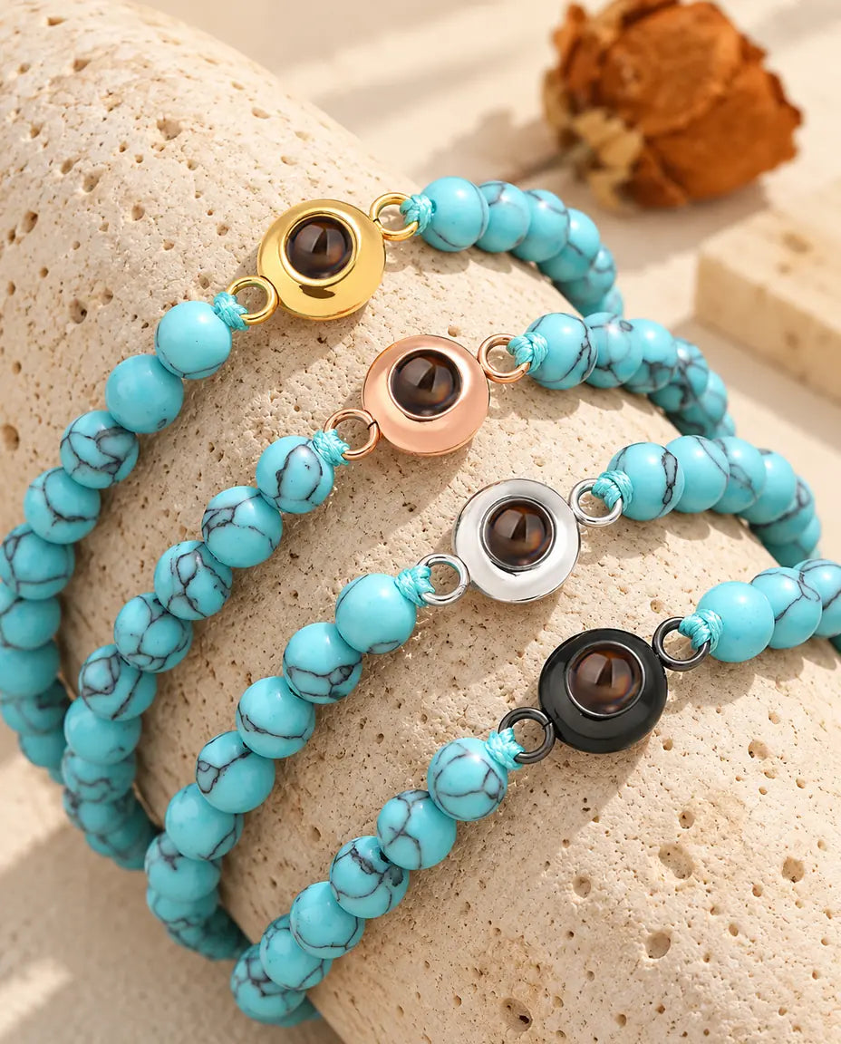 Vier blauw gemarmerde kralenarmbanden met foto erin, goudkleurig, roségoudkleurig, zilverkleurig en zwart, op travertijn