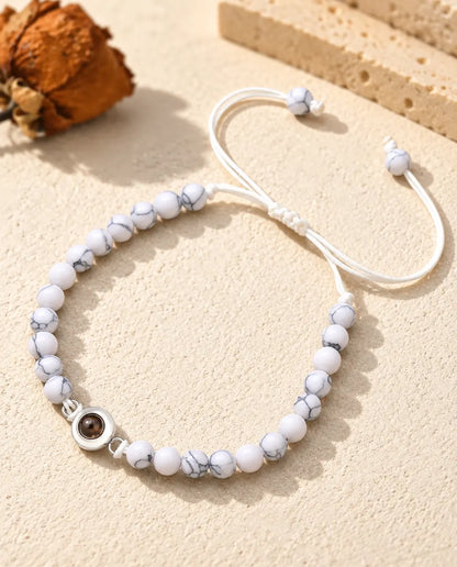 Wit gemarmerde kralenarmband met een zilverkleurige ringbedel met foto erin en een schuifknoop