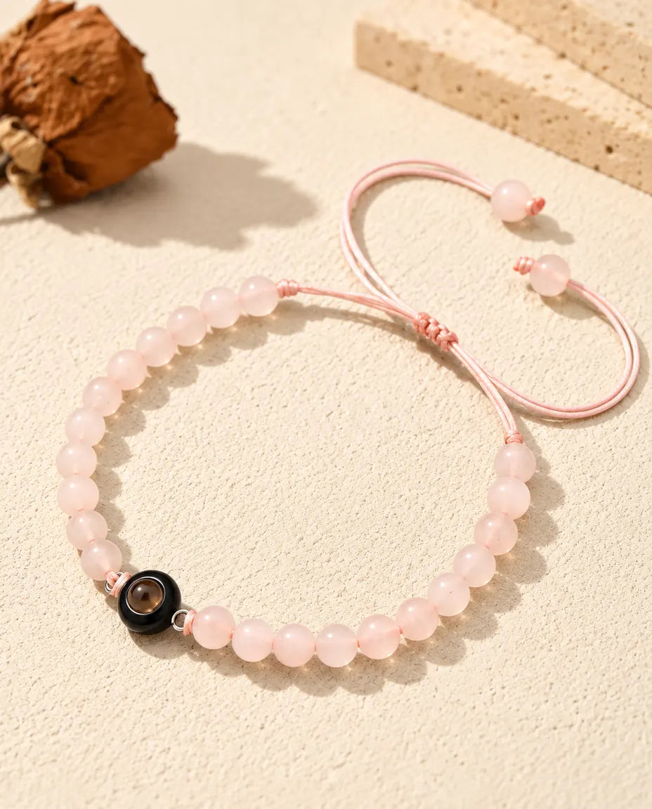 Lichtroze kralenarmband met een zwarte ringbedel met projectiesteentje op crèmekleurig gips