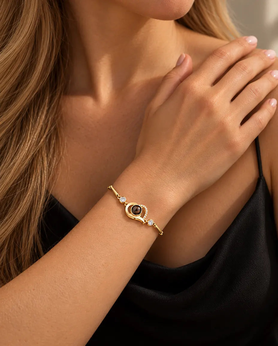 Close-up van de goudkleurige armband met open hartje en zirkonia om een pols bij het sleutelbeen