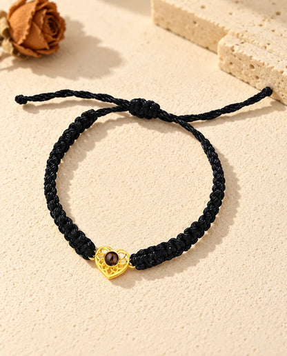 Bovenaanzicht van de armband met een goudkleurig hartje aan zwart koord, met schuifknoop en uiteinden