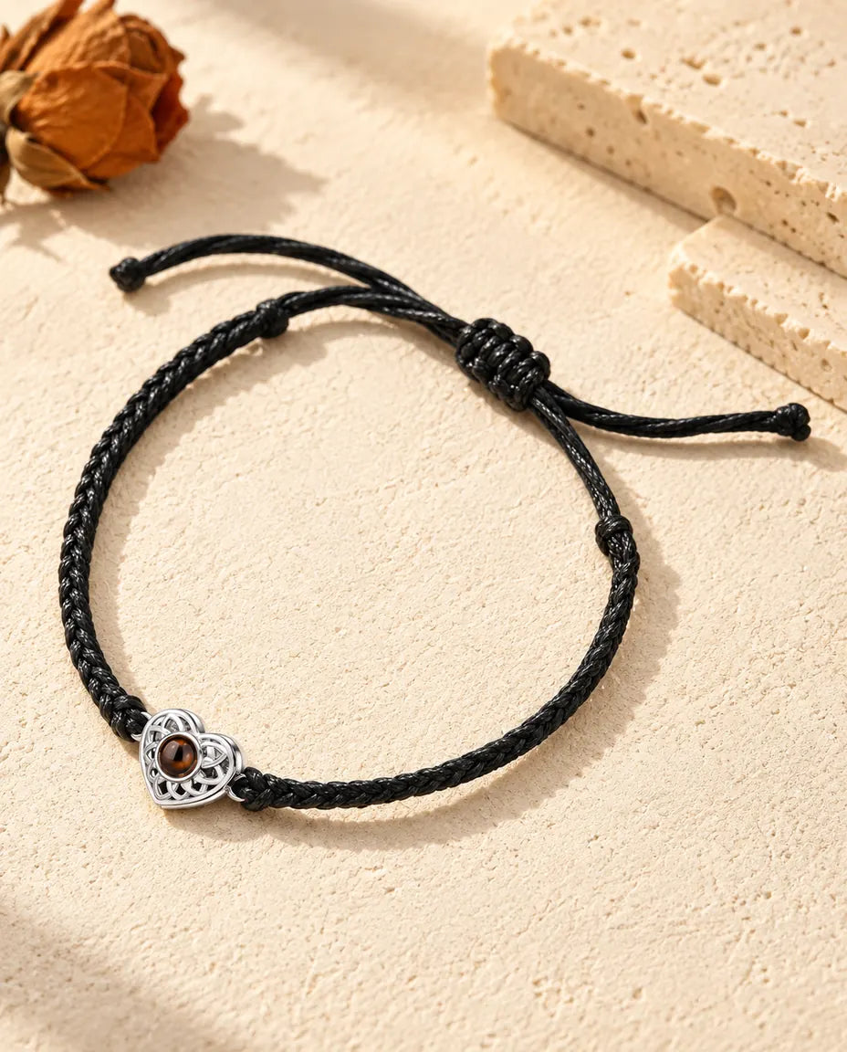 Armband met foto erin: opengewerkt zilverkleurig hartje aan een zwart, dun gevlochten koord, op crèmekleurig gips