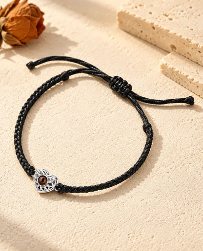Armband met foto erin: opengewerkt zilverkleurig hartje aan een zwart, dun gevlochten koord, op crèmekleurig gips