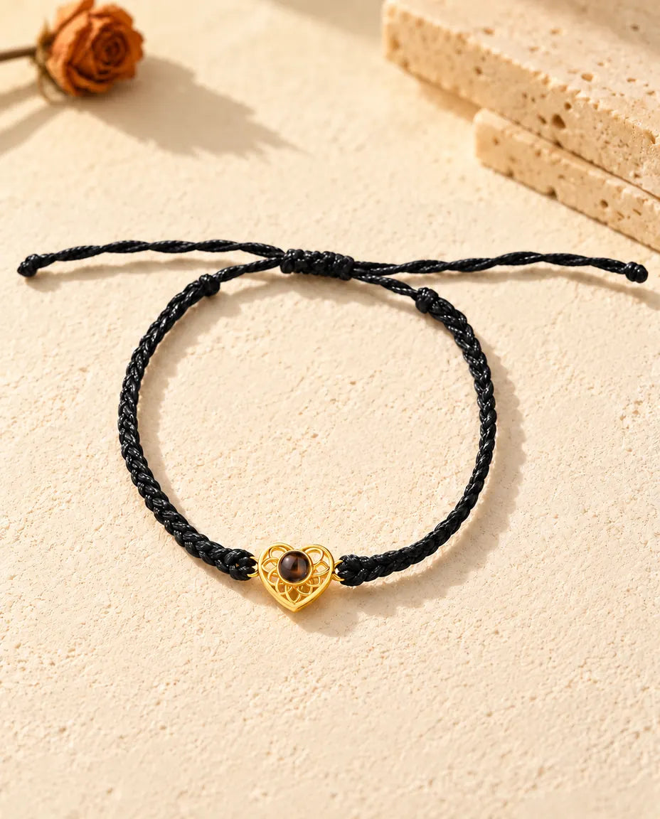 Bovenaanzicht van de armband met een goudkleurig hartje aan zwart koord, met schuifknoop en uiteinden