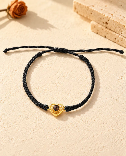 Bovenaanzicht van de armband met een goudkleurig hartje aan zwart koord, met schuifknoop en uiteinden