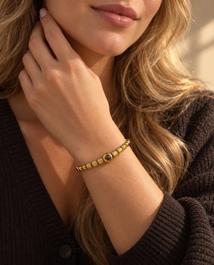 Vrouw raakt de zijkant van haar hals aan en draagt de goudkleurige kralenarmband met foto erin