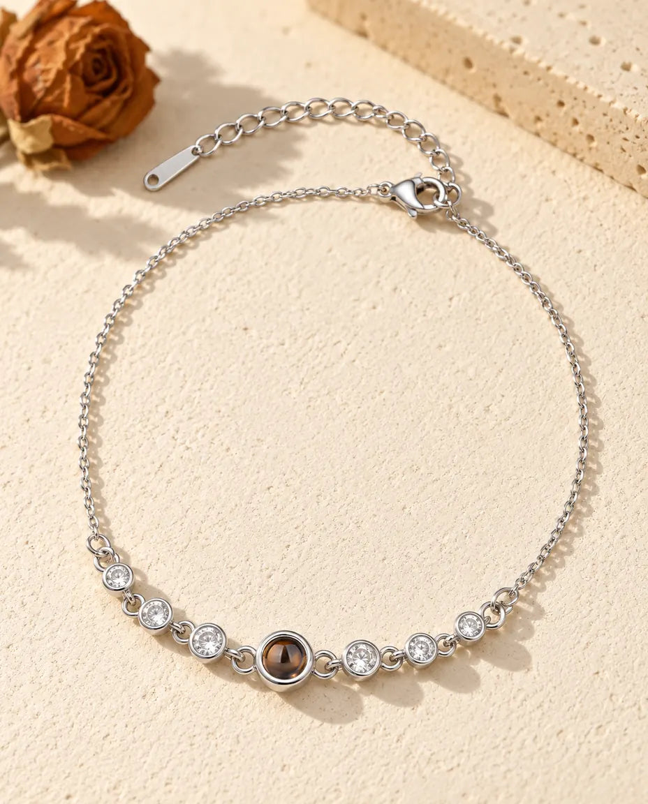 Armband met foto erin: zilverkleurig rijtje zirkonia aan een fijne ketting, liggend op crèmekleurig gips