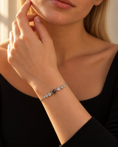 Vrouw raakt haar kaaklijn aan en draagt de zilverkleurige armband met foto erin en het rijtje zirkonia