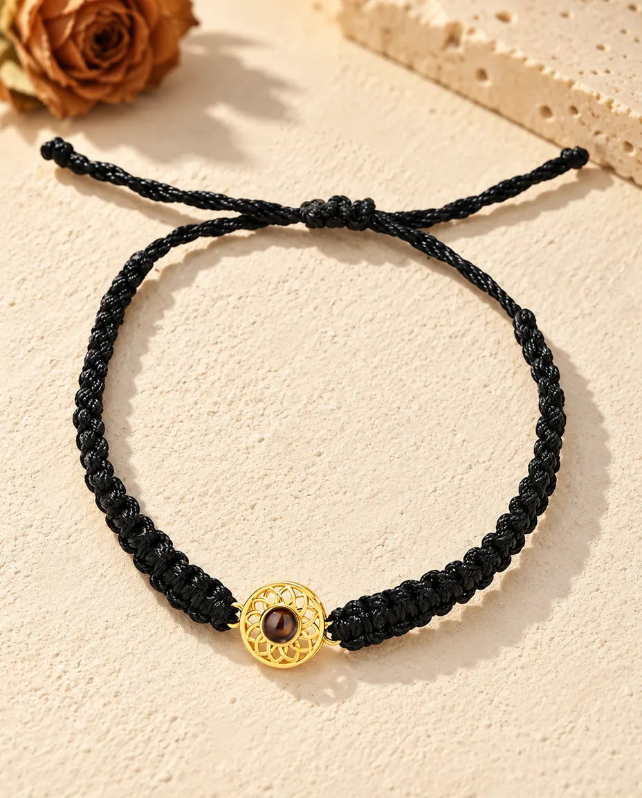Bovenaanzicht van de armband met een goudkleurige ronde bedel aan zwart koord, met schuifknoop en uiteinden
