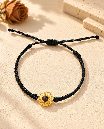 Bovenaanzicht van de armband met een goudkleurige ronde bedel aan zwart koord, met schuifknoop en uiteinden