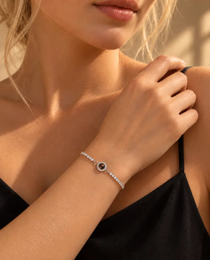 Vrouw met haar hand op haar schouder draagt de zilverkleurige tennisarmband met halo-bedel en foto erin