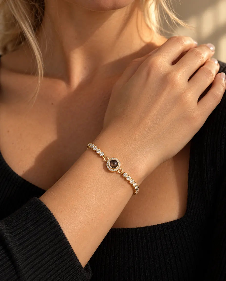Close-up van de goudkleurige tennisarmband met halo-bedel om een pols bij het sleutelbeen