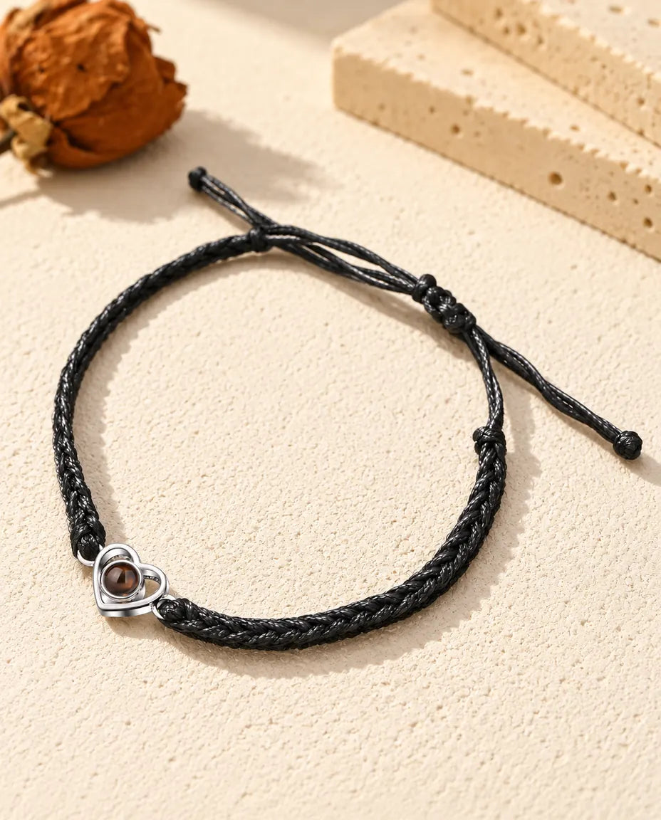 Armband met foto erin: open hartje van 925 sterling zilver aan een zwart gevlochten koord, op crèmekleurig gips