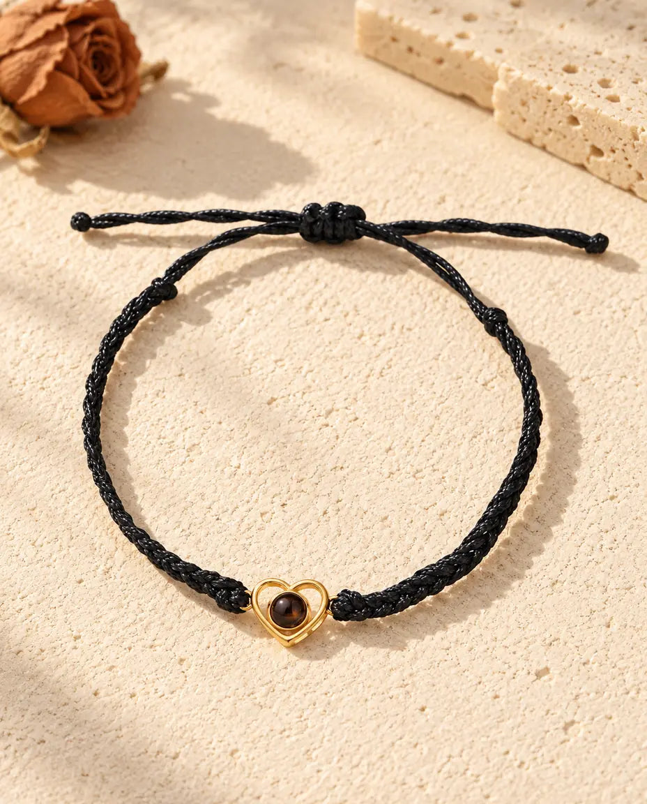 Bovenaanzicht van de armband met goudkleurig open hartje aan een zwart gevlochten koord en de schuifknoop