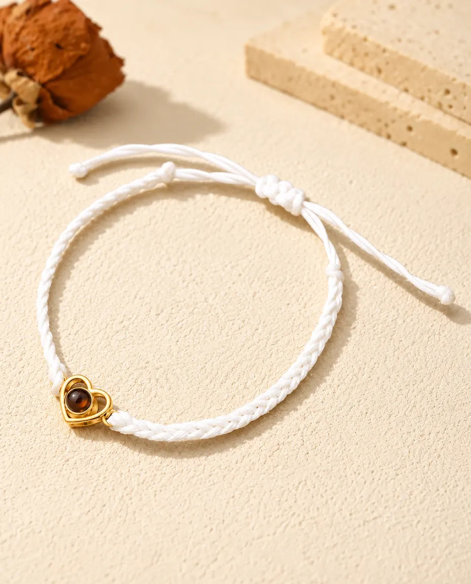 Armband met foto erin aan een wit gevlochten koord met goudkleurig open hartje en schuifknoop