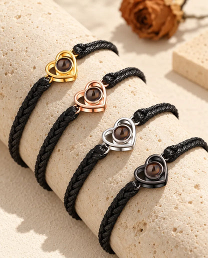 Vier zwarte gevlochten armbanden met een open hartje in elke kleur op een blok travertijn