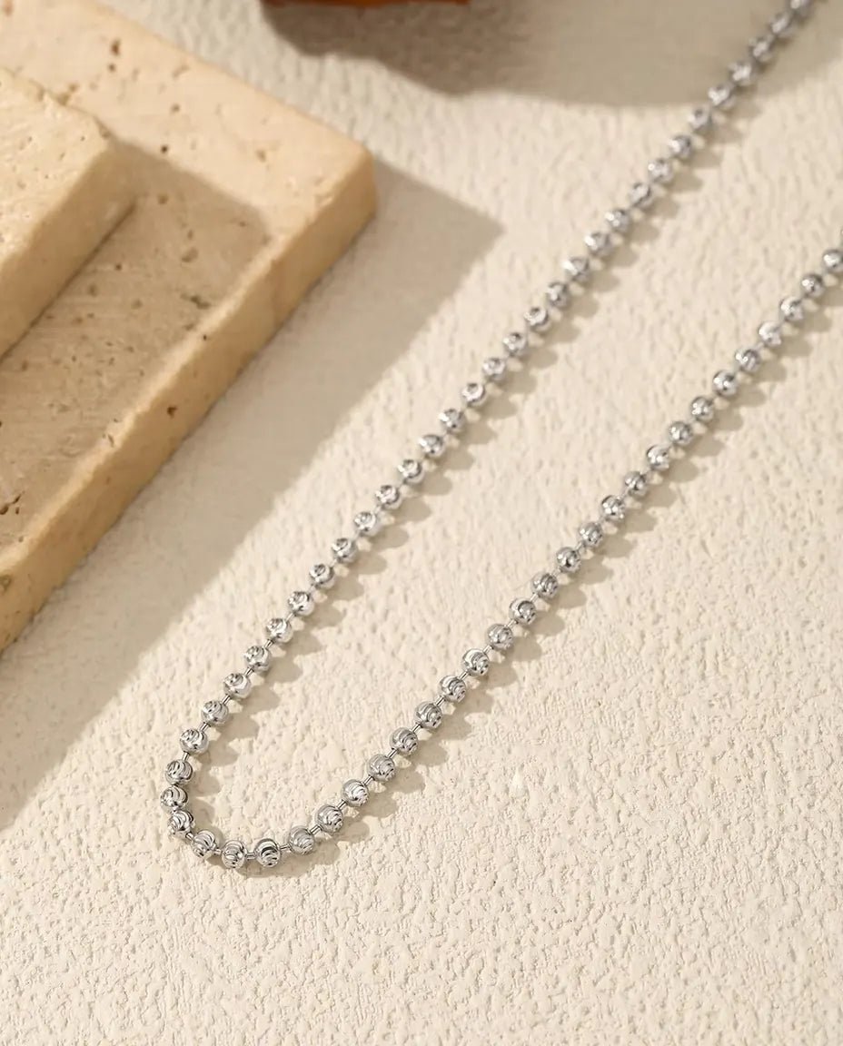 Ketting met Gefacetteerde Kralen in 925 Sterling Zilver - op een licht oppervlak naast een travertijnplaat