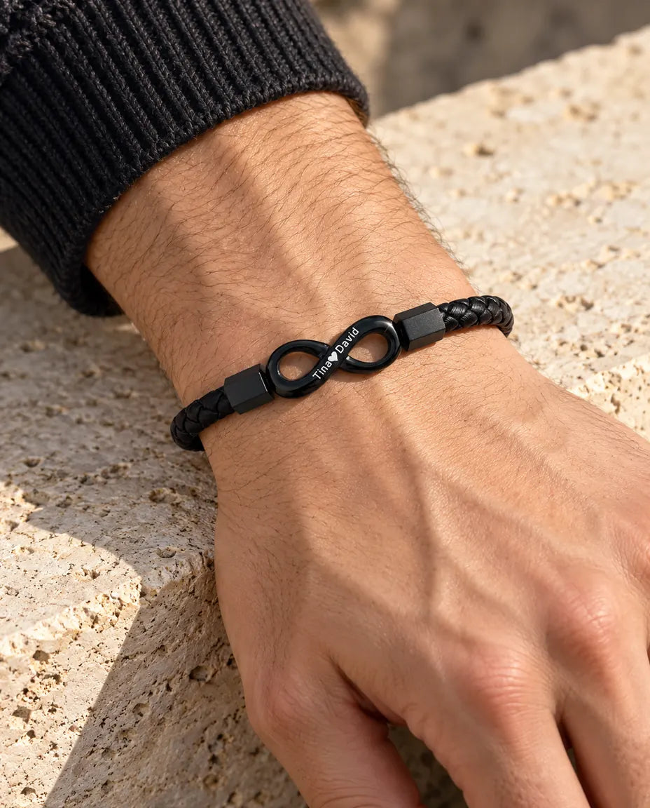 Man draagt de zwarte gegraveerde armband met oneindigheidsteken en gevlochten kunstleer bij een antraciet gebreide trui