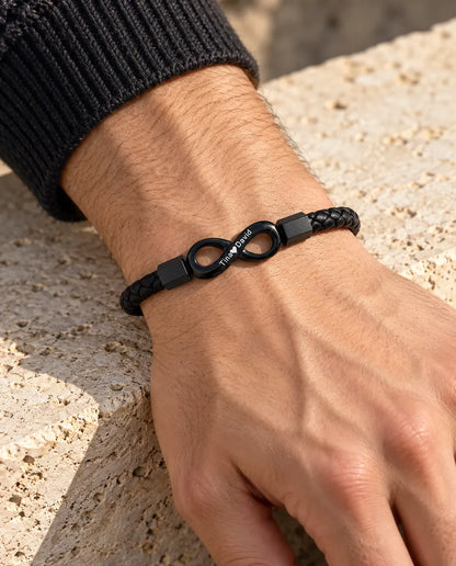 Man draagt de zwarte gegraveerde armband met oneindigheidsteken en gevlochten kunstleer bij een antraciet gebreide trui