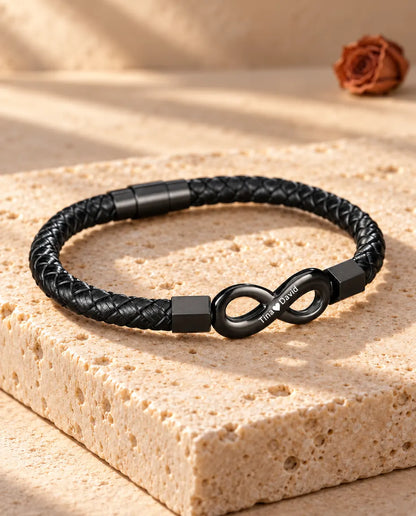 Driekwart aanzicht van de gegraveerde herenarmband met oneindigheidsteken en magnetische cilindersluiting op travertijn