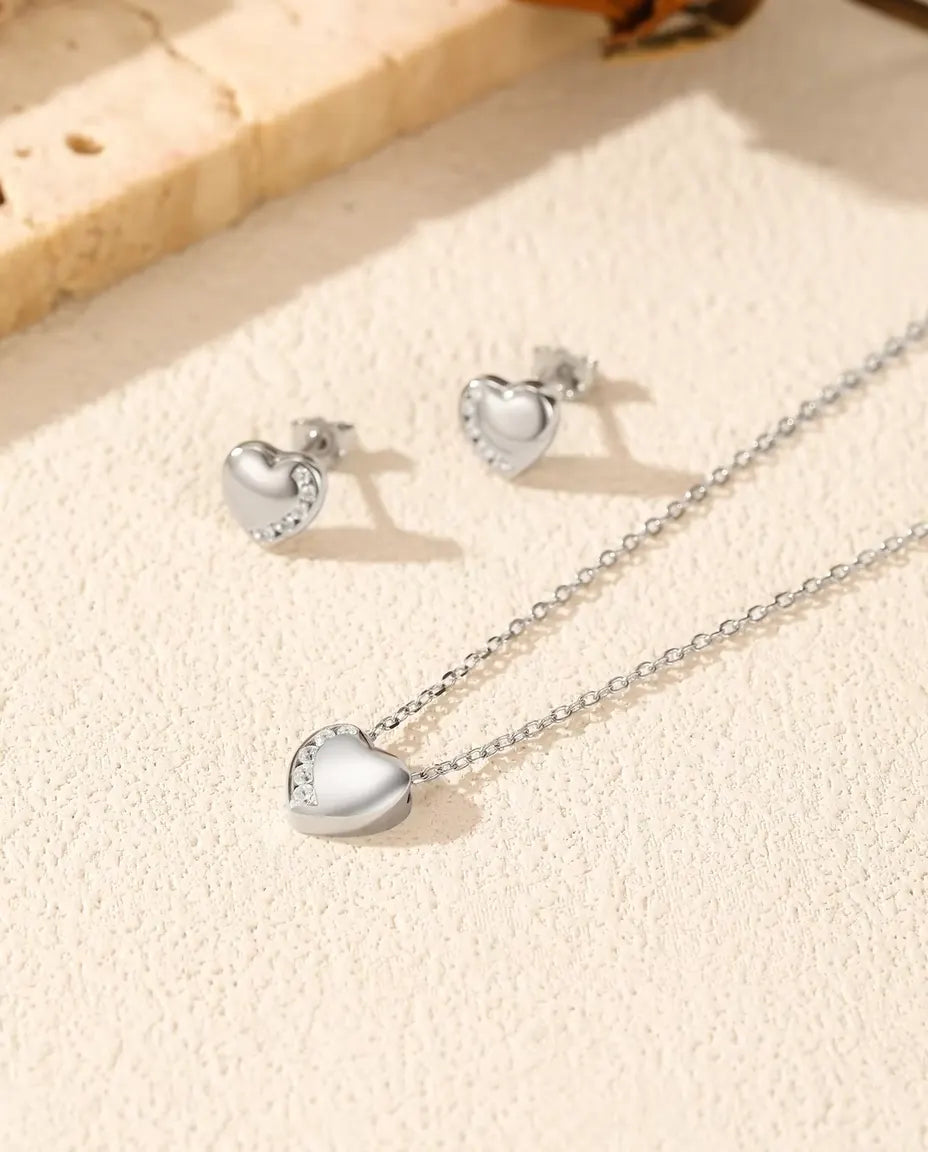 Hartjes Sieradenset in 925 Sterling Zilver - ketting en oorbellen samen op een licht gestructureerd oppervlak