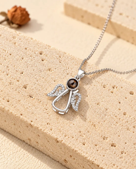 Gepersonaliseerde zilverkleurige ketting met foto erin in de vorm van een beschermengeltje, op travertijn