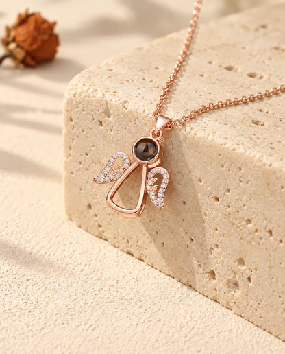 Roségoudkleurige ketting met engeltje en foto erin over travertijn gedrapeerd